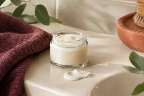 Soin après-shampooing transparent pour boucles posé dans une salle de bain ivoire, prune et terre cuite.