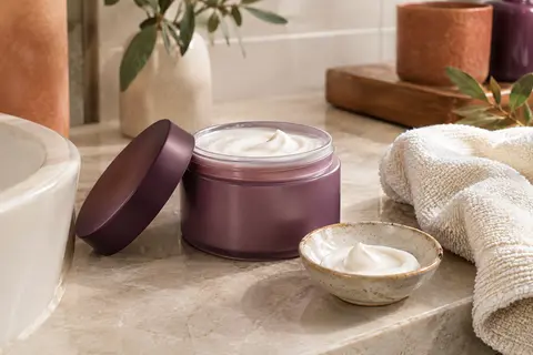 Crème coiffante Cantu présentée dans une salle de bain claire, avec une coupelle en céramique et un linge en coton.