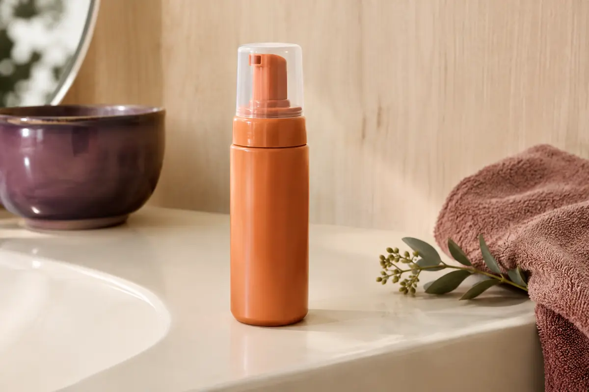 Contenant orange de mousse coiffante à l’huile d’argan posé dans une salle de bain lumineuse.