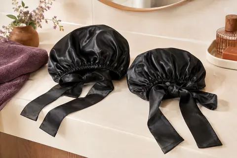 Deux bonnets noirs en satin à longues bandes réglables, posés sur une tablette ivoire dans une salle de bain