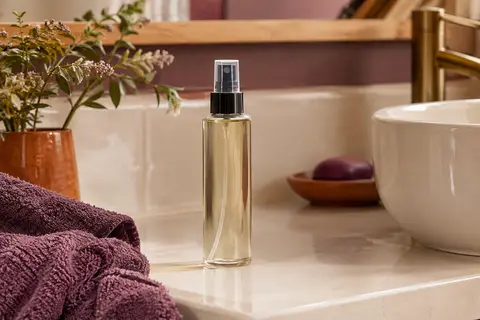 Flacon de spray coiffant posé sur une tablette en céramique dans une salle de bain lumineuse aux tons doux.