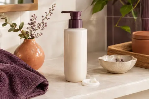 Flacon de crème définissante pour boucles posé dans une salle de bain lumineuse aux tons ivoire et terre cuite